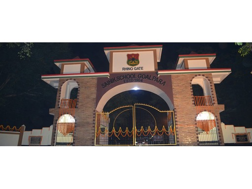 Wide-angle view of Sainik School Goalpara, Assam, with its sprawling campus nestled in a lush green landscape. The school’s buildings, sports grounds, and pathways are visible, with students in uniforms engaged in activities, surrounded by scenic hills and a calm, disciplined atmosphere.