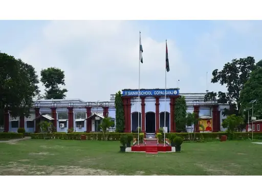 View of Sainik School Gopalganj, Bihar, showcasing its expansive campus with modern academic buildings, sports fields, and well-kept grounds. Students in military uniforms are seen walking or engaged in outdoor activities, surrounded by green fields and a peaceful, disciplined environment.