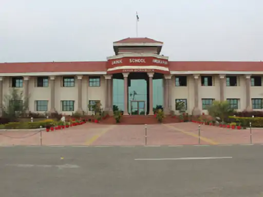 Aerial view of Sainik School Amravati, showing its sprawling campus with well-maintained lawns, modern buildings, and a central parade ground. Students in uniform are seen walking across the pathways, with the backdrop of hills and green landscapes surrounding the school.